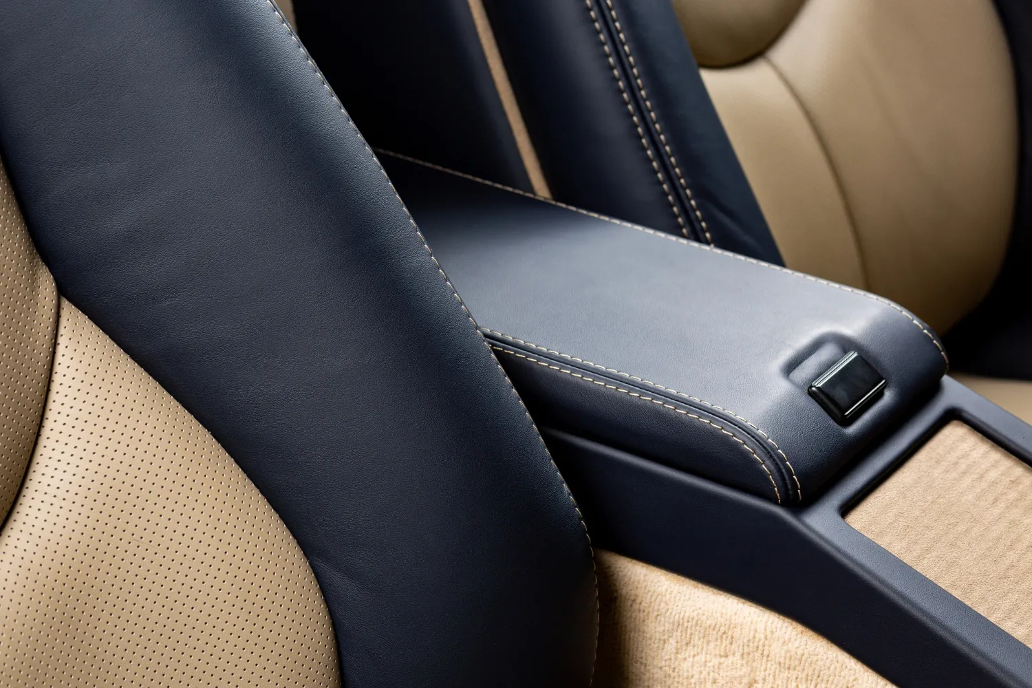 Detalle del interior de un automóvil que muestra un reposabrazos de cuero negro y asientos de cuero beige, resaltando la comodidad y el diseño elegante del vehículo.