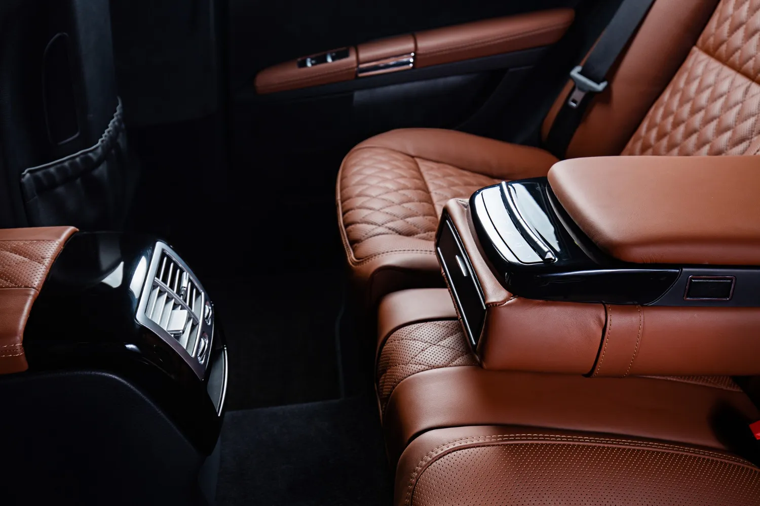 Interior de un automóvil de lujo con asientos de cuero marrón y detalles elegantes. Se observa un reposabrazos central con controles de climatización y un diseño moderno.